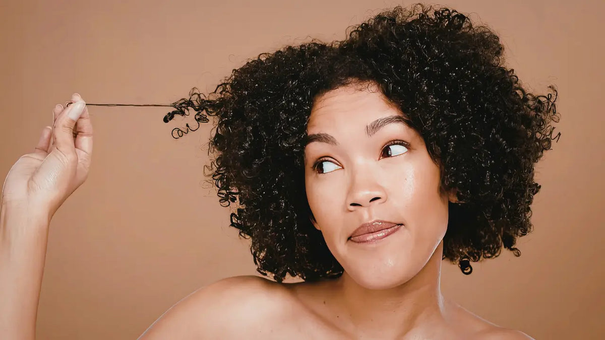 Woman with defined natural curls gently stretching one curl to show texture, elasticity, and stronger-looking curl definition.